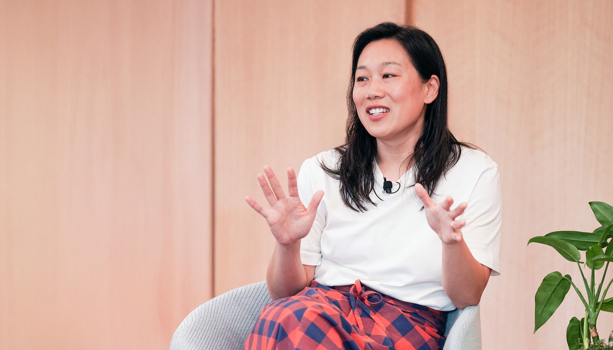 Priscilla Chan sits in a chair and gestures with her hands. She wears a black and red checkered skirt and a white T-shirt.