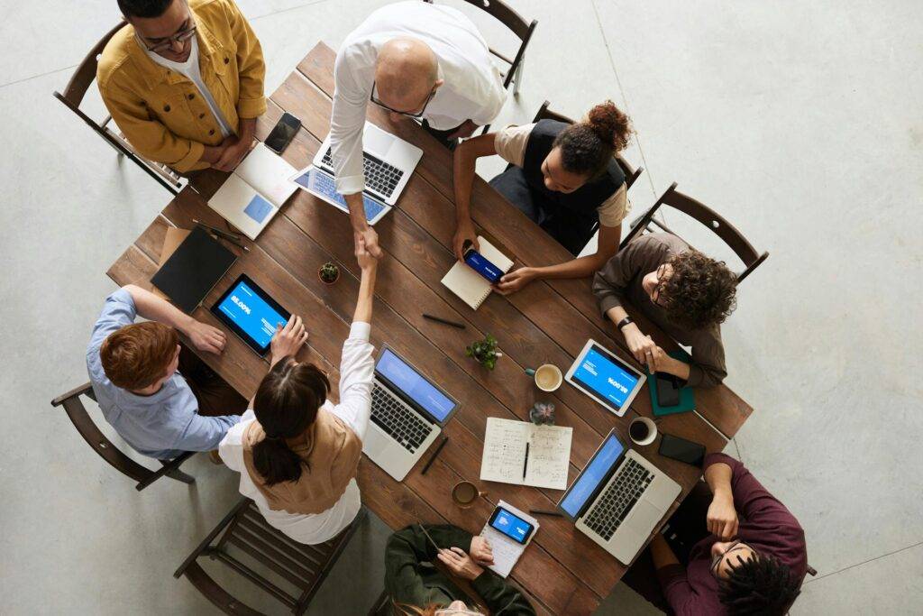 a Group of Stakeholders Sitting Around a Wooden Table, Shaking Hands, Representing the Benefits of Knowing How to Document Technical Requirements through a Technical Requirements Document