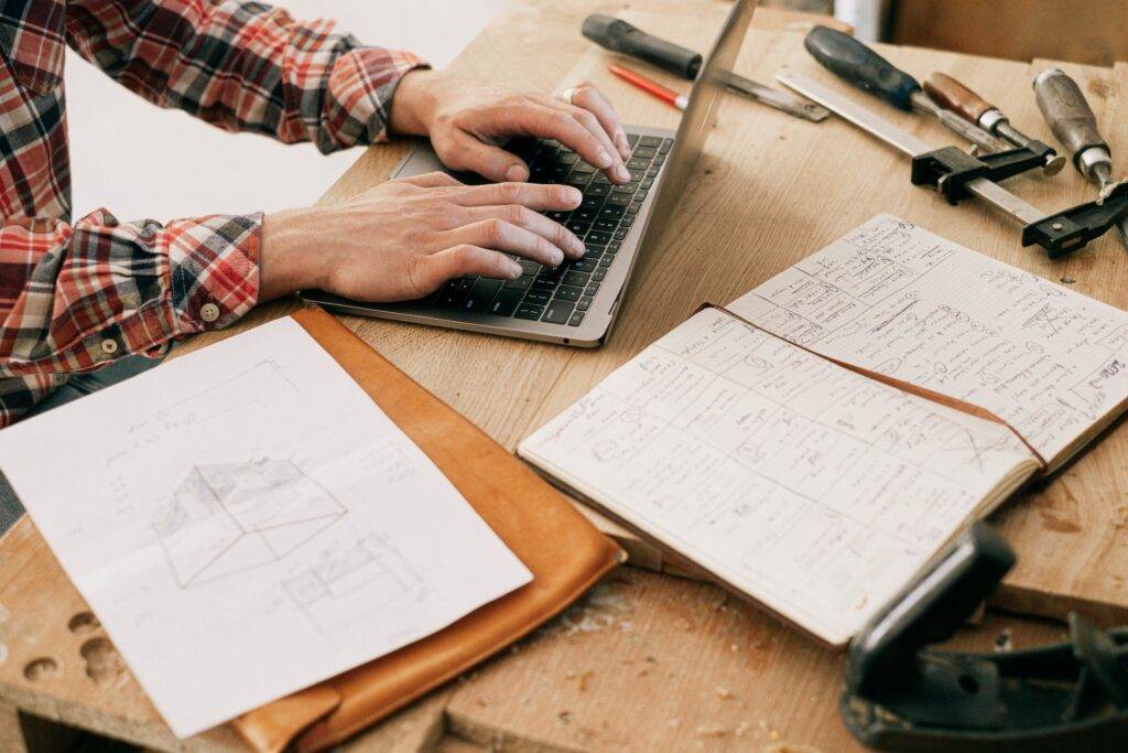 A Person Typing on a Laptop while Sitting at a Work Bench, Representing the Importance of Manufacturing Technical Writers